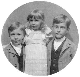 A vintage circular portrait of two young boys flanking a young girl in formal period clothing, reflecting the history of Bischwind Villa.