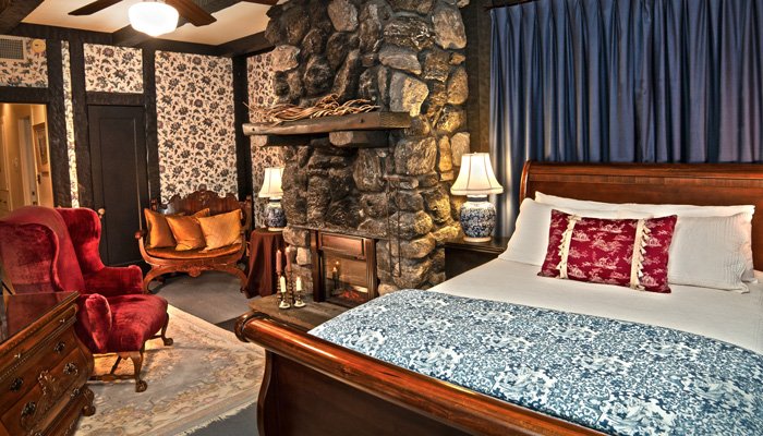 A hotel bedroom with a large stone fireplace, a queen-sized bed, and a red velvet armchair.